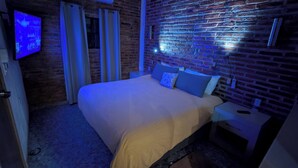 Une chambre d’hôtel avec un mur en briques, un lit avec une literie blanche, un téléviseur fixé au mur et une table de chevet.