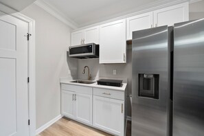 A modern kitchen with white cabinets, stainless steel appliances, and a wooden floor.