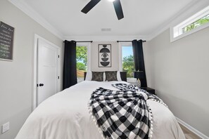 A bedroom with a bed, a ceiling fan, a window with curtains, and a wall art piece.