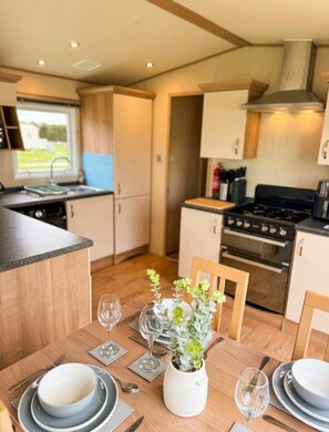 A compact kitchen with a dining area, a window, and a view of the outdoors. - Fantasy Island Resort, The Sunnydale C6 Eastgate - Coastal Caravan Breaks (Ingoldmells)
