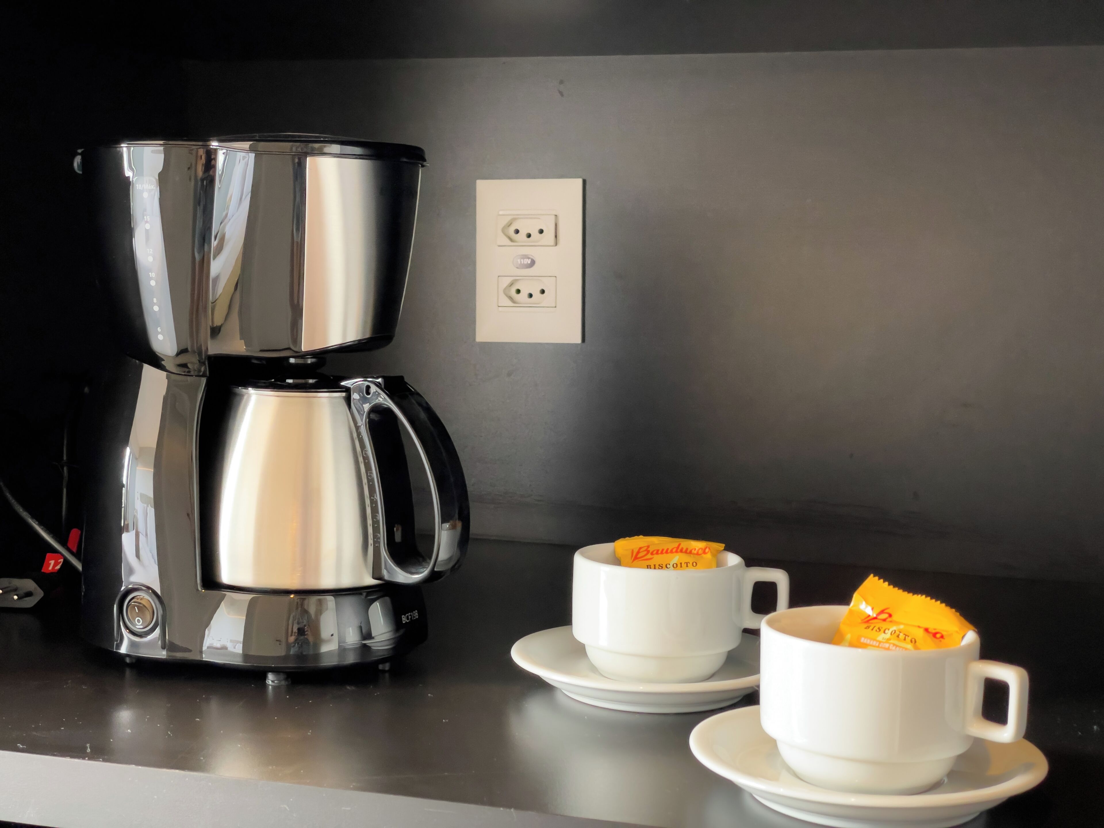 Una cafetera sobre una encimera con dos tazas blancas y un paquete de galletas.