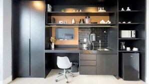 A modern kitchen with a built-in oven, microwave, and coffee maker, a white chair, and a black countertop. - VN Alvorada (São Paulo)