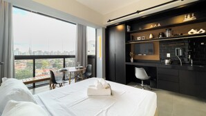 A modern hotel room with a large bed, a dining area, a kitchen, and a city view. - VN Alvorada (São Paulo)