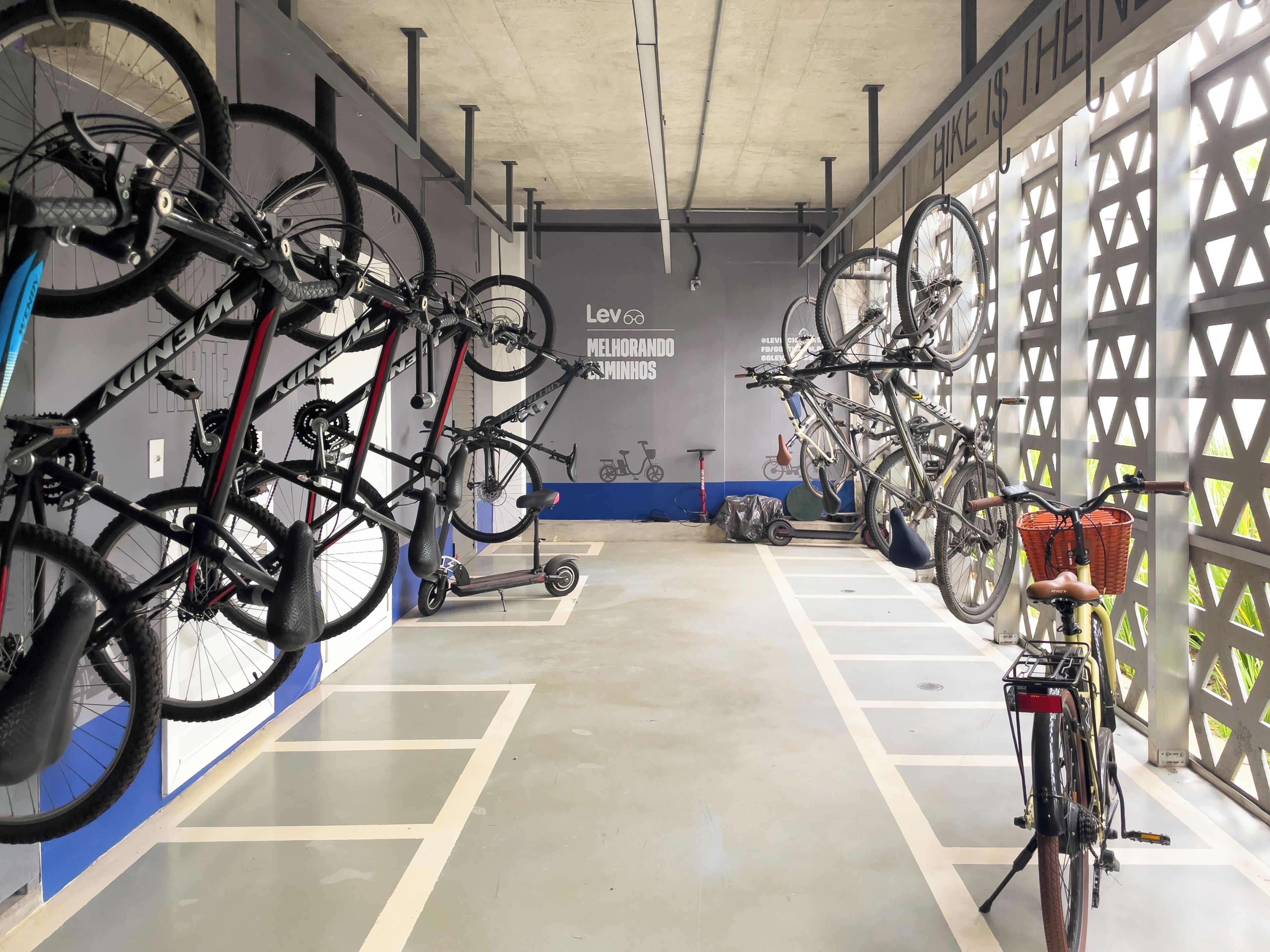 A bike storage area with multiple bicycles and a scooter, a concrete floor, and a wall with a cycling-related mural.