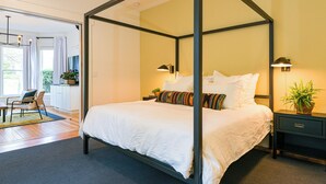A four-poster bed with white linens, a bedside table with a lamp, and a potted plant. - Suite 1 at Kubli Haus - Luxury, Style & Location, 1 block to Britt (Jacksonville)