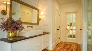A bathroom with a large mirror, a sink, and a vase of flowers. - Suite 4 at Kubli Haus<br>Luxury, Style & Location, 1 block to Britt (Jacksonville)