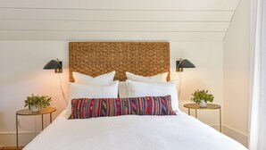 A bed with white bedding, a woven headboard, two bedside lamps, and two small tables with plants. - Suite 4 at Kubli Haus<br>Luxury, Style & Location, 1 block to Britt (Jacksonville)