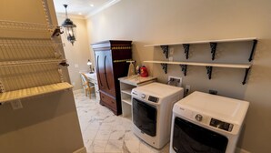A laundry room with two washing machines, a cabinet, and shelves. - Marymount College Building (Salina)
