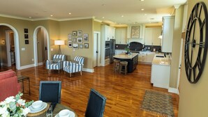 A spacious living room with a dining area, kitchen, and a large clock on the wall. - Marymount College Building (Salina)