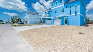 A two-story residential building with a blue exterior, a front garage, and a clear sky. - Shore Bet (Fort Myers Beach)