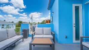 A blue building with a white door, a grey outdoor sofa, and a wooden table. - Shore Bet (Fort Myers Beach)