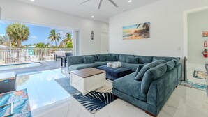 A modern living room with a sectional sofa, a ceiling fan, a painting, and a view of the outdoors. - Shore Bet (Fort Myers Beach)