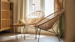 A room with two wicker chairs, a small table, a wooden cabinet, and a large vase with pampas grass.