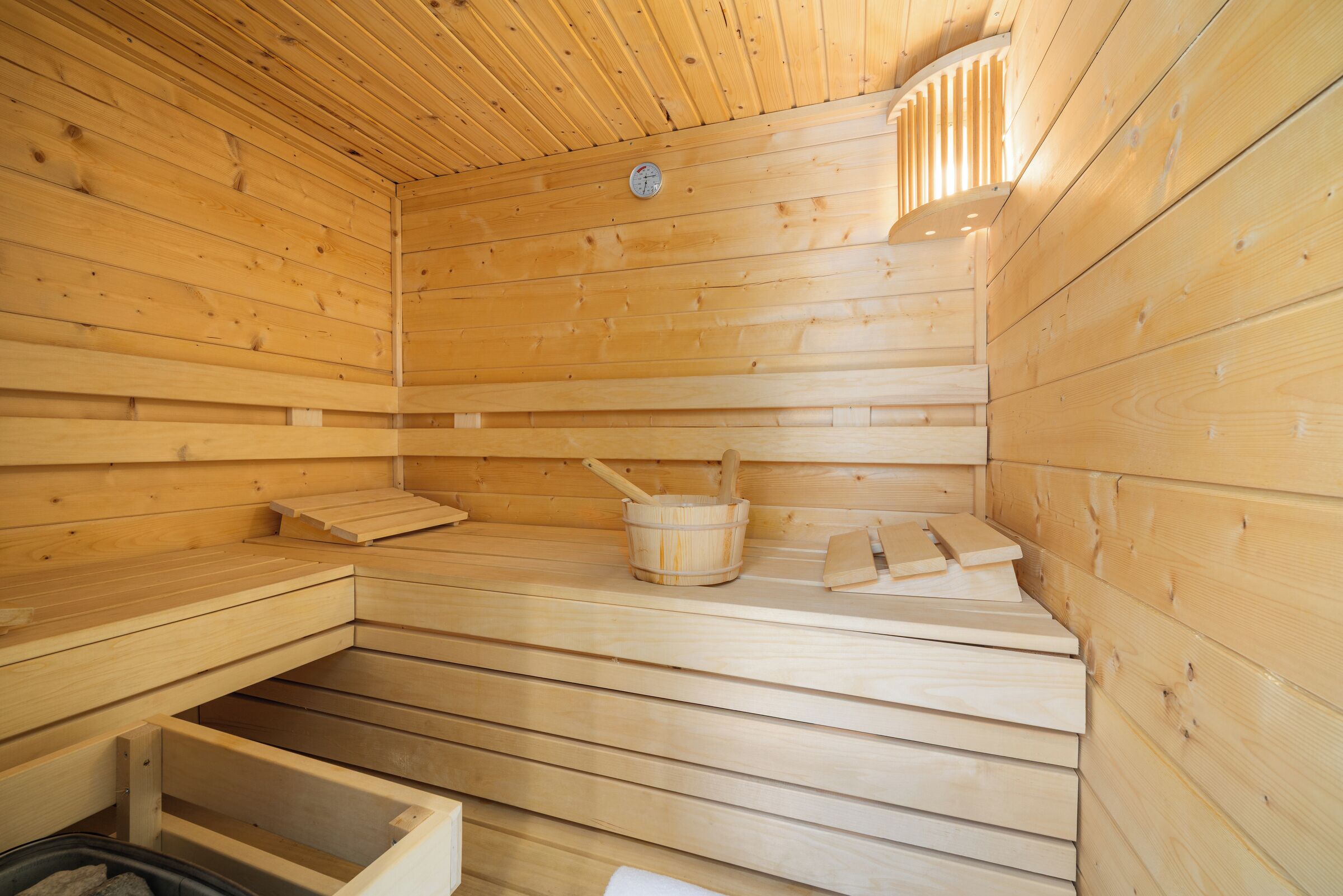 A wooden sauna with benches, a bucket, and a wooden bench.