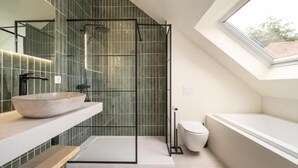 A modern bathroom with a skylight, a freestanding bathtub, a glass-enclosed shower, and a large mirror.