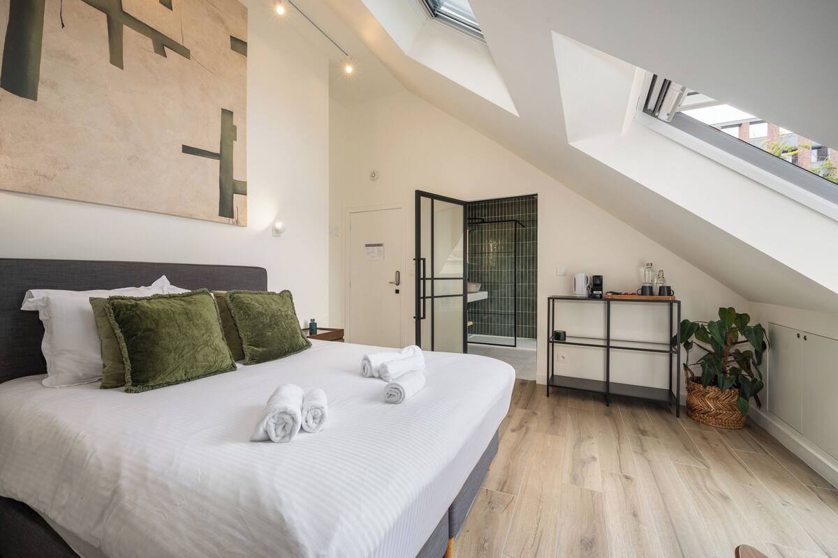 Un dormitorio moderno con una cama grande, tragaluz, una kitchenette pequeña y vistas al exterior.