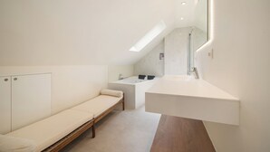 A modern bathroom with a skylight, a bench, a bathtub, and a sink.