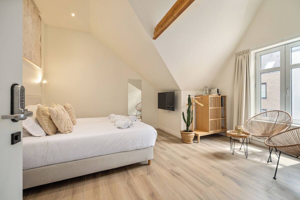 Un dormitorio con cama, televisor, aparador de madera, una silla y ventana.