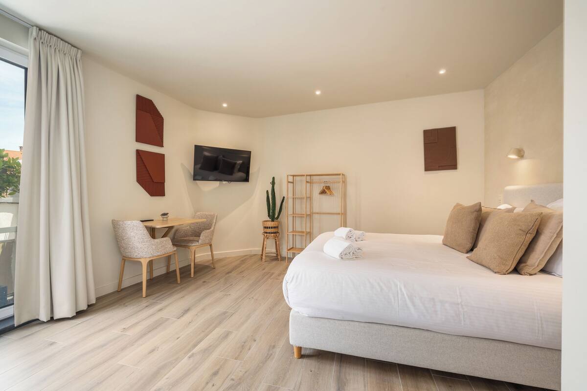 Habitación de hotel con cama, escritorio, silla, televisor, un cactus y ventana con cortinas.