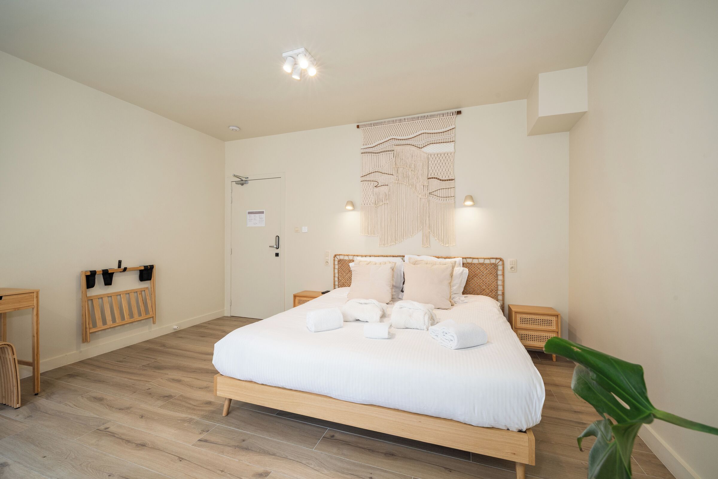 Une chambre bien rangée, avec un lit, des tables de chevet, un luminaire fixé au mur et une porte.