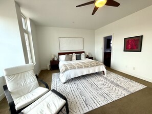 Ein Schlafzimmer mit Bett, Stuhl, Deckenventilator, Teppich und Bildern an der Wand.
