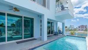 A modern building with a swimming pool, large glass doors, and a balcony with outdoor furniture. - Beach Please (Fort Myers Beach)
