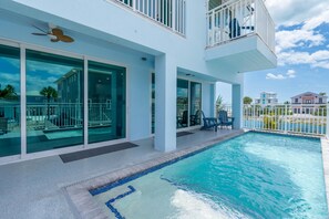 A modern building with a swimming pool, large glass doors, and a balcony with outdoor furniture. - Beach Please (Fort Myers Beach)