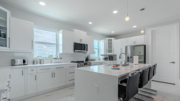 A modern kitchen with white cabinetry, a central island with seating, a microwave, stove, and refrigerator. - Beach Please (Fort Myers Beach)