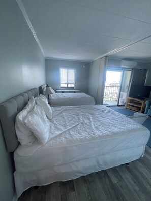 A hotel room with two beds, a window with blinds, an air conditioning unit, and a television. - Cute 1-bedroom apt 23rd St in Ocean City near the beach (Ocean City)