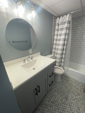 A bathroom with a round mirror, a sink, a toilet, and a shower curtain. - Cute 1-bedroom apt 23rd St in Ocean City near the beach (Ocean City)