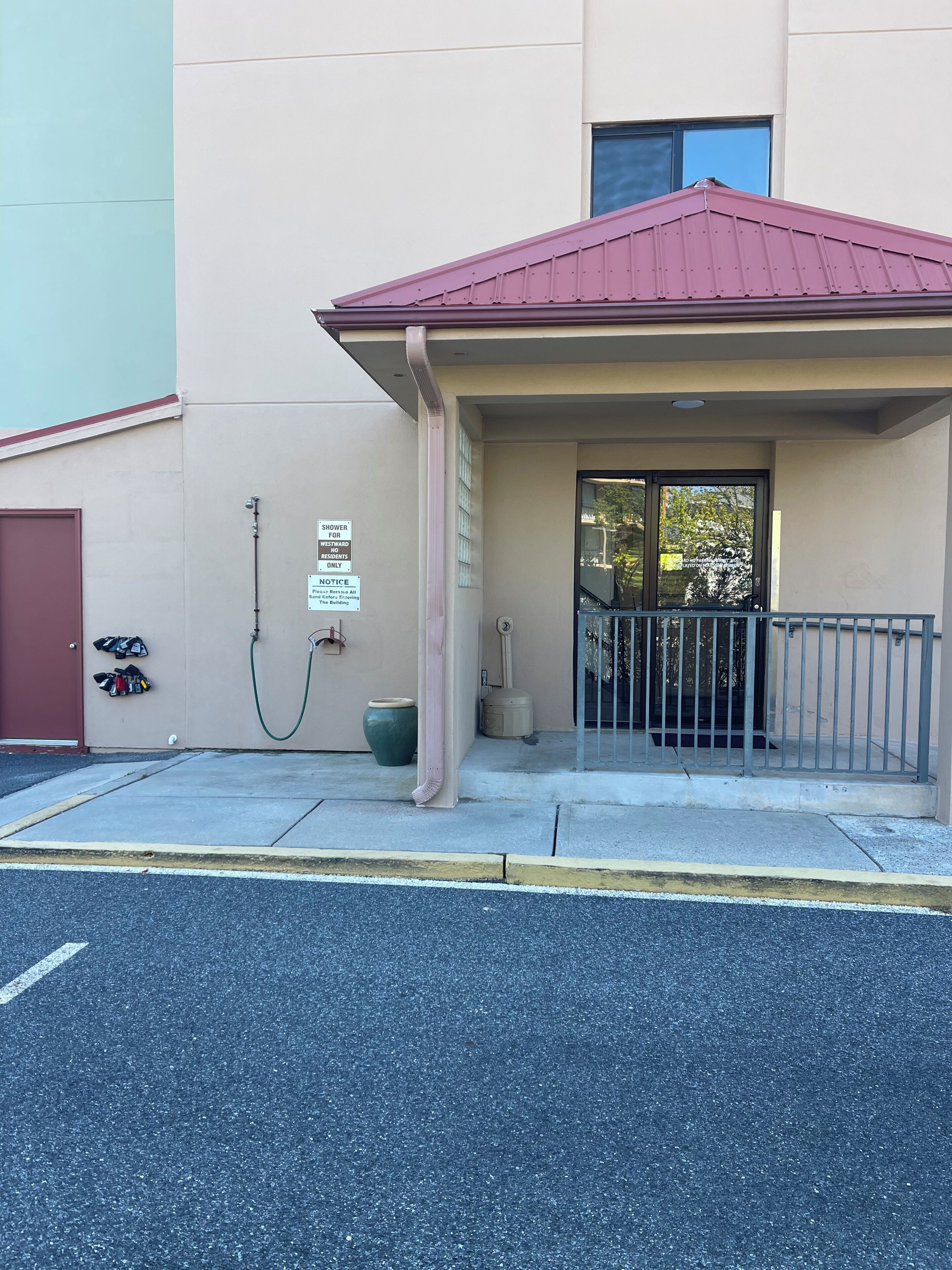 A building with a red roof, a covered entrance, a sign indicating a shower for westward-facing residences, and a pair of shoes on the wall.