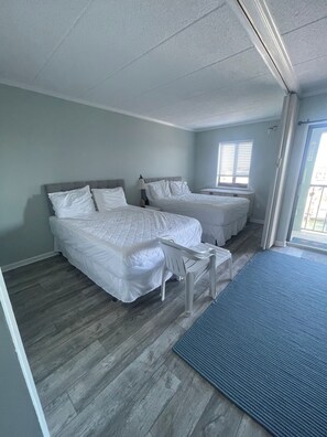 A room with two beds, a small table, and a window with blinds. - Cute 1-bedroom apt 23rd St in Ocean City near the beach (Ocean City)