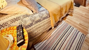 Une pièce aux murs lambrissés, avec un lit, un téléviseur fixé au mur et une petite table sur laquelle se trouve une télécommande.