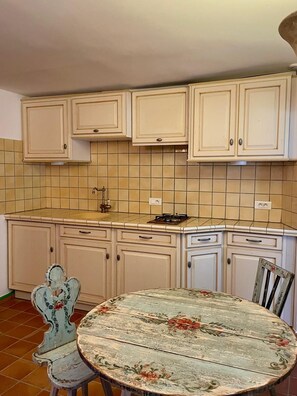 Uma cozinha com armários brancos, painel de azulejos, fogão a gás e uma mesa redonda com cadeiras estampadas.