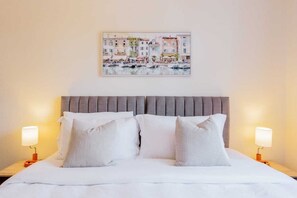 A hotel room with a bed, two pillows, a headboard, a nightstand, and a wall-mounted painting.
