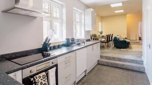 A modern kitchen with white cabinets, a black countertop, and a dining area with a sofa and table. - Contractor and Business Stays | Sleeps 6 | WiFi (Hertfordshire)