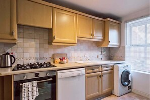 A kitchen with beige cabinets, a stove, oven, dishwasher, and a washing machine. - Contractor-Hub Home | Close to MK & M1 (Wolverton)