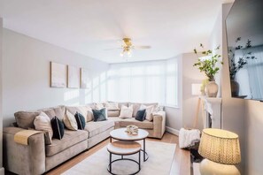 Ein Wohnzimmer mit einem beigefarbenen Ecksofa, einem runden Couchtisch und einem Deckenventilator.