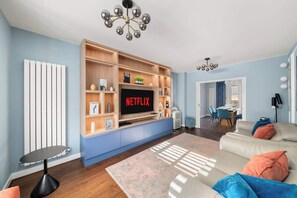 A modern living room with a flat-screen TV, wooden shelving, a sofa, and a dining area. - Sleeps 6 | Relocation & Long Stays, FREE Parking (Greater London)