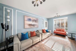 A living room with a beige sofa set, a painting on the wall, a chandelier, and a window with blinds. - Sleeps 6 | Relocation & Long Stays, FREE Parking (Greater London)