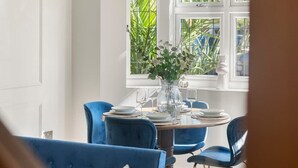 A dining area with a round table, blue upholstered chairs, and a window with a view of greenery. - Contractor Friendly 3BR | Driveway Parking | WiFi (Greater London)