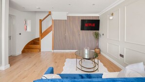 A modern living room with a staircase, a mounted TV, and a round glass table. - Contractor Friendly 3BR | Driveway Parking | WiFi (Greater London)
