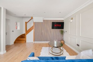 A modern living room with a staircase, a mounted TV, and a round glass table. - Contractor Friendly 3BR | Driveway Parking | WiFi (Greater London)