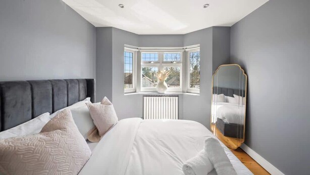 A bedroom with a bed, a window, a radiator, and a mirror. - Contractor Friendly 3BR | Driveway Parking | WiFi (Greater London)