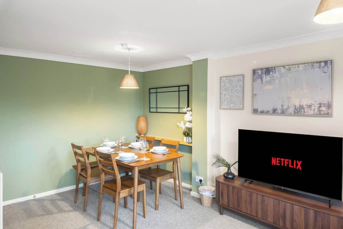 Een eethoek met een tafel gedekt voor vier personen, een televisie waarop het Netflix logo te zien is, en een aan de muur hangend schilderij.