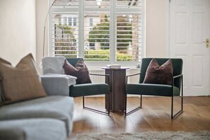 Ein Wohnzimmer mit einer Couch, zwei Sesseln, einem kleinen Tisch und einem Fenster mit Jalousien.