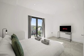 A modern hotel room with a large bed, a television, and a view through the window. - Modern 4BR Home, Ideal for Long Stays & Relocation (Greater London)