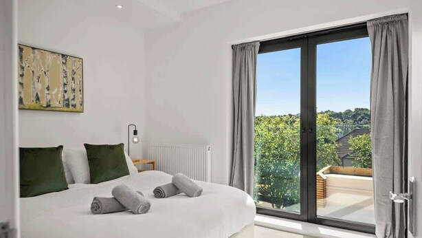 Une chambre avec un grand lit, un radiateur, une fenêtre avec des rideaux et une vue sur la verdure.