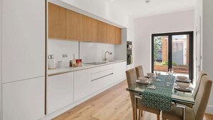 Une cuisine moderne avec des meubles blancs, un élément supérieur en bois et un coin repas comprenant une table et des chaises en verre.