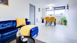 Un salon moderne avec un canapé bleu, des coussins jaunes, un coin repas avec des chaises jaunes et une grande fenêtre donnant sur un beau paysage.